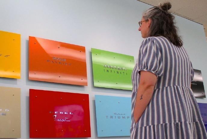 A woman wearing a striped dress views a colorful wall display of metallic plaques.