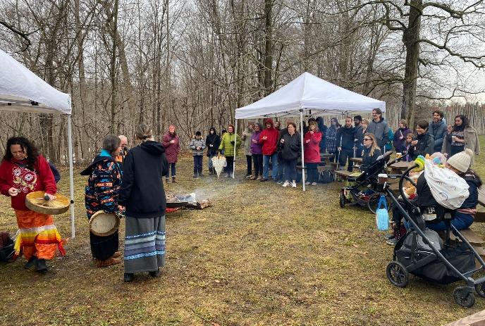 Group of people under a canopy watching an Indigenous display outside of the Museum of Ontario Archaeology.