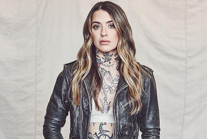 Morgan Wade in a leather jacket and ripped jeans, standing confidently against a beige backdrop.