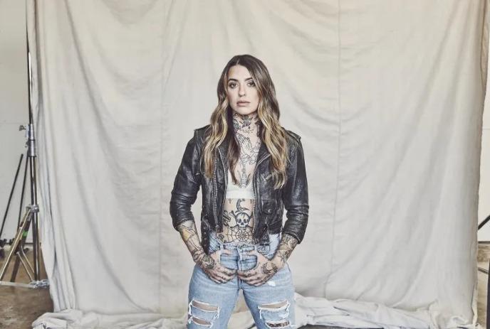 Morgan Wade in a leather jacket and ripped jeans, standing confidently against a beige backdrop.