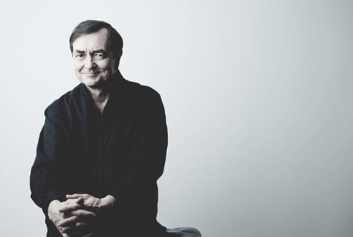 Artist sitting calmly with a smile under a soft lighting and gray backdrop evoke quiet contemplation.