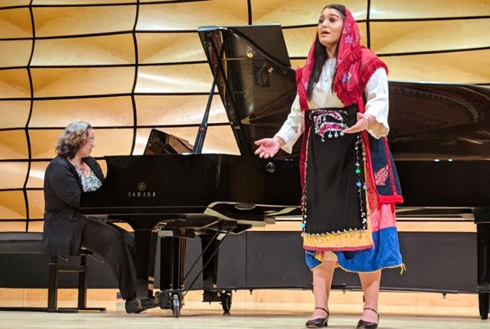 A performer sings beside a pianist at a grand piano.