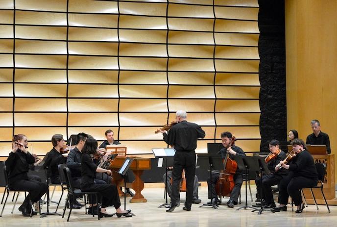 Group of musicians playing instruments on stage with a warm background.