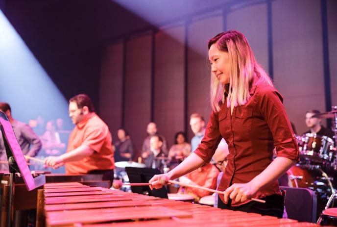 Musicians in red play marimbas onstage with other people and artists in the background.