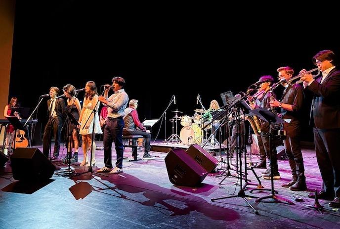 Musicians standing and performing on stage with dark purple lighting.