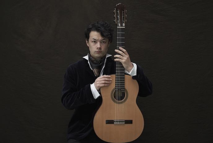 Stoic person sits with their guitar in front of them.