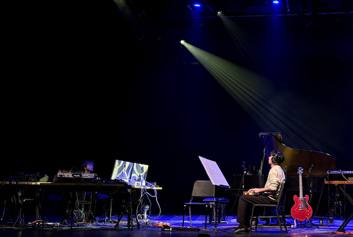 Open stage with one person wearing headphones sitting in the middle by a red guitar.