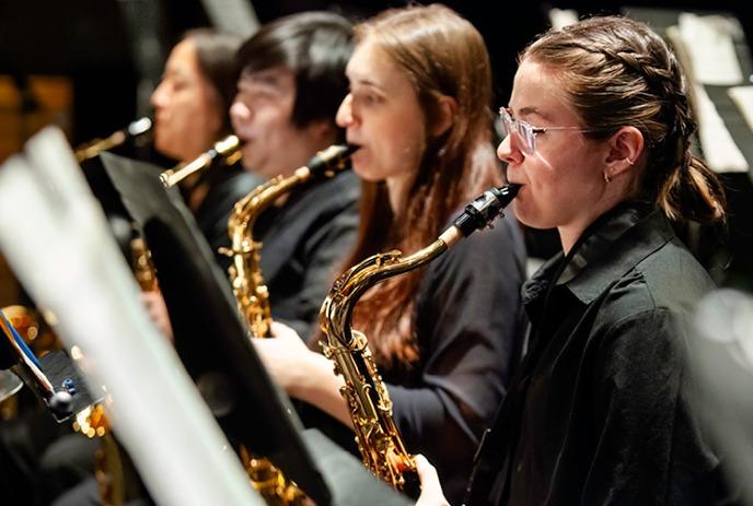 A group of four musicians playing saxophones in a concert setting, all wearing black attire.