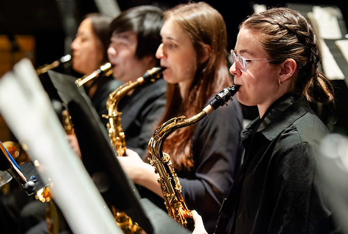 Four people stand playing their wind instruments together.