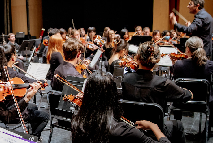 An orchestra plays their instruments while watching the conducter.
