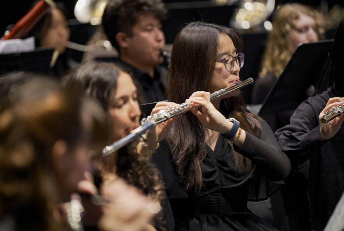 A focused group of musicians plays flutes in a concert, each wearing black attire.