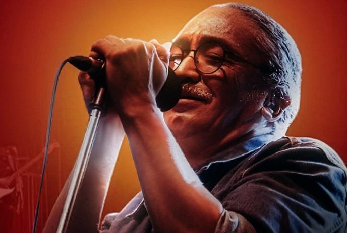 A man passionately sings into a microphone against a vibrant red background with musical notes and waveforms.