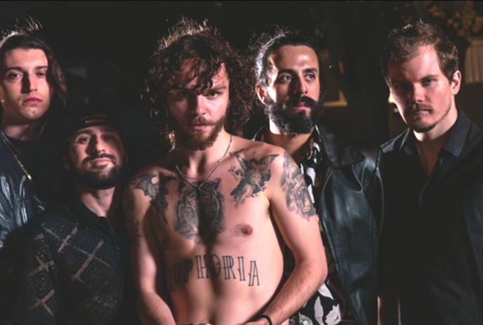 Five band artists stand together, with one tattooed person shirtless under a dark background.