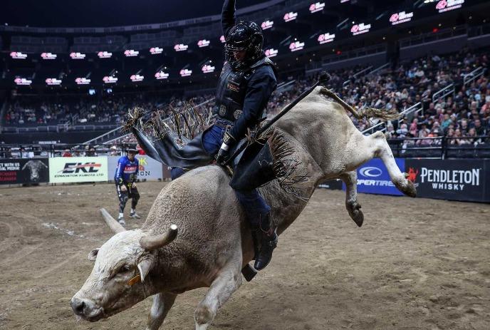 A man riding a thrashing white bull in a bull pen in front of a large crowd.