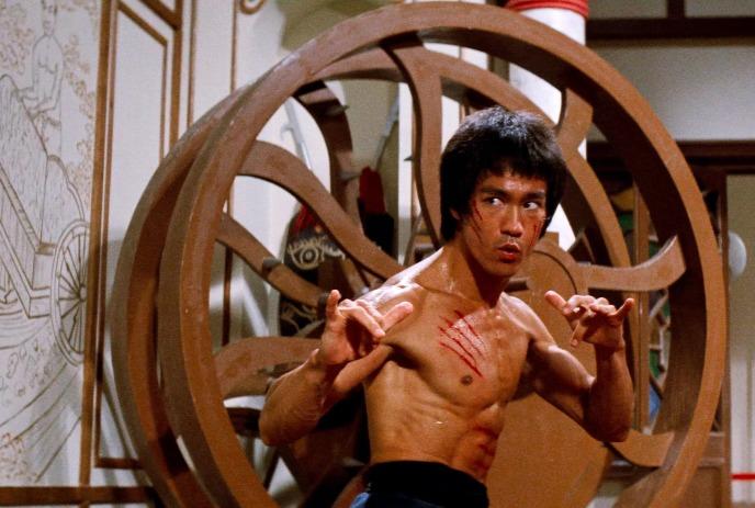 Martial artist stands shirtless in wooden hall poised to fight with fierce focus and marked chest.