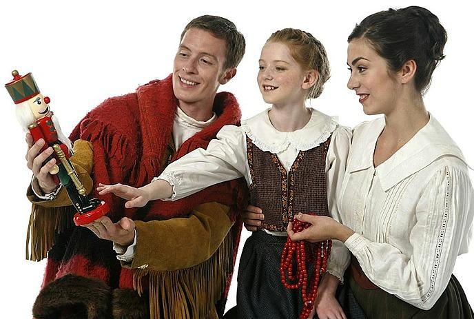 A smiling family admires a colorful nutcracker, sharing a joyful holiday moment together in traditional attire.