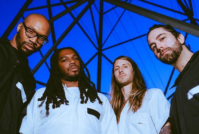 The OBGMs looking down at the camera, with a dark blue sky and beams behind them.