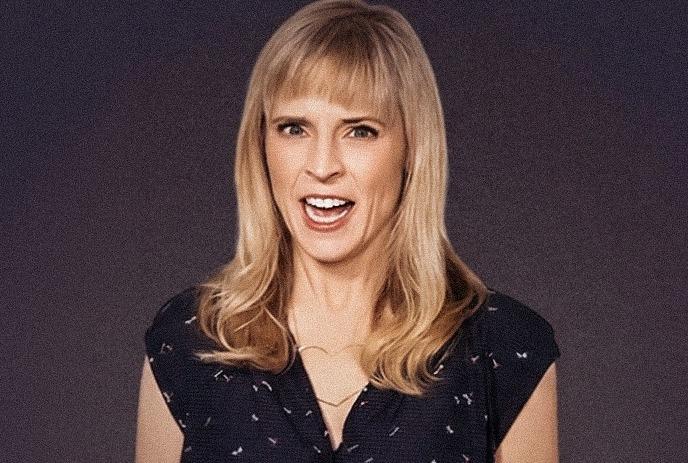 Maria Bamford against dark background wearing patterned shirt under a dark background.