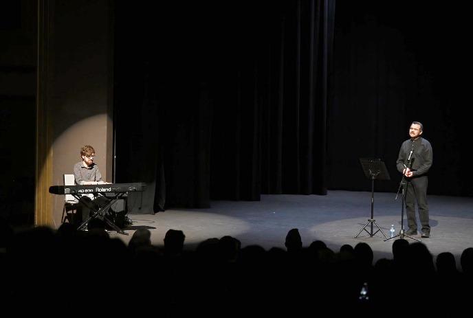Keyboard player and vocalist performing on dim stage as seated audience watches the live musical act.