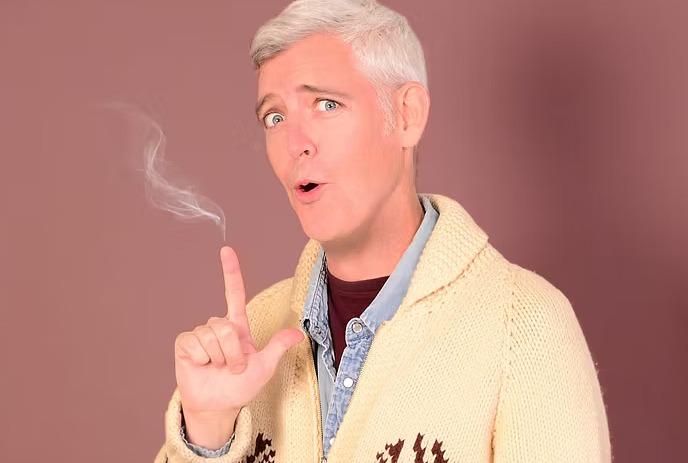 Person in yellow sweater holds up smoking finger with surprised look, set against a red and yellow background.
