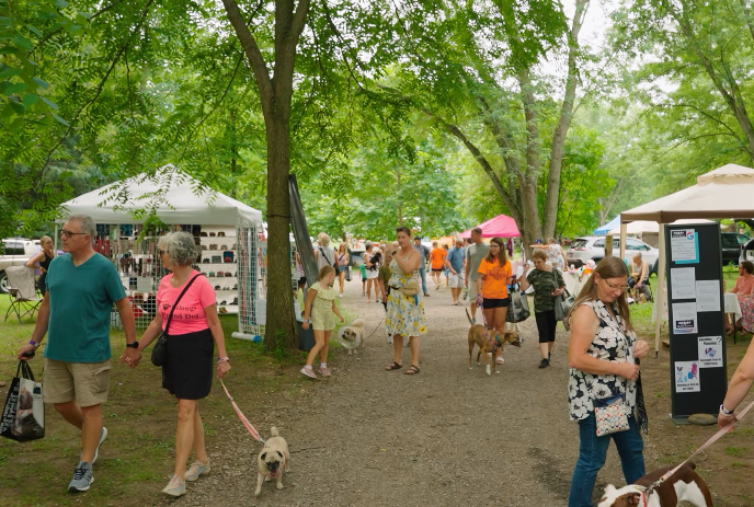 People and their dogs enjoying a previous Pawsitively Elgin Dog Festival outdoors in a park.
