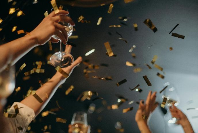 People raising glasses of champagne with golden confetti falling in a festive celebration.