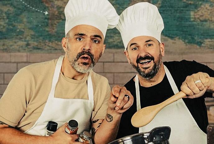 Two people wearing chef hats and aprons stand together looking forwards.