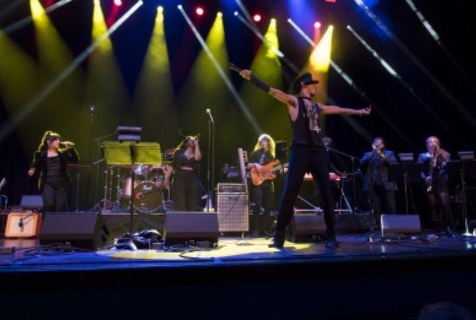 Classic Albums Live band performs on stage with the lead singer in a black hat under colorful lights.
