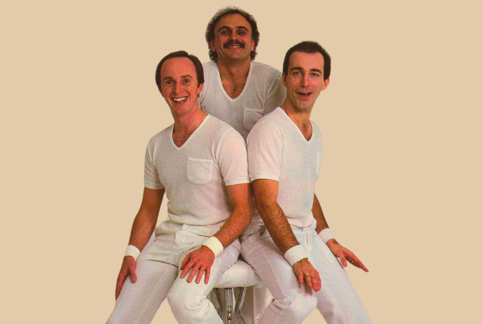 Three people wearing white, posing around a stool.