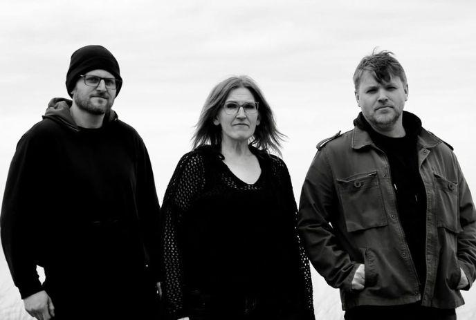 Three artists standing outdoors in black and white against a cloudy sky background scene.