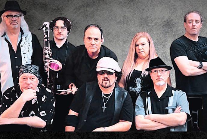 Eight artists pose together with hats sunglasses and saxophone against neutral gray backdrop.