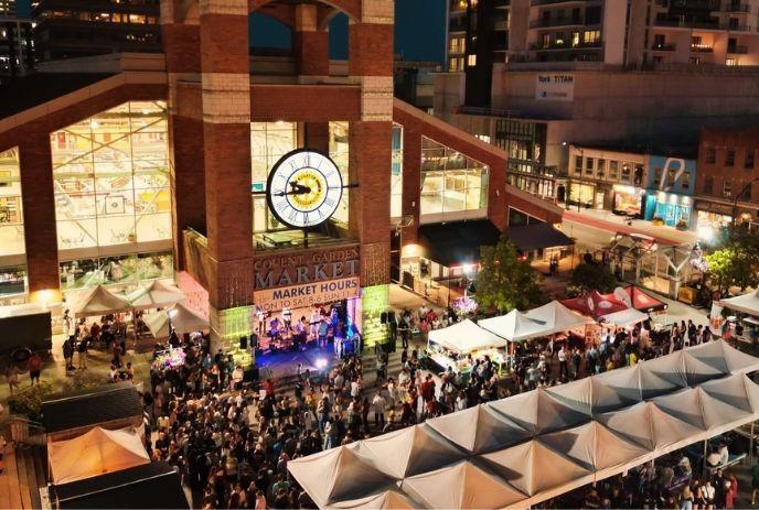 Night crowd gathered at Covent Market with tents stage and clocktower building glowing.