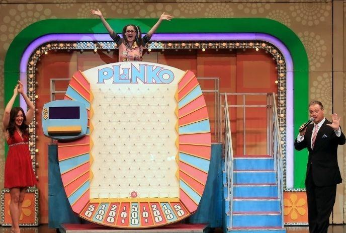 Giant Plinko game board on stage with three people celebrating, arms raised, in a colorful set.