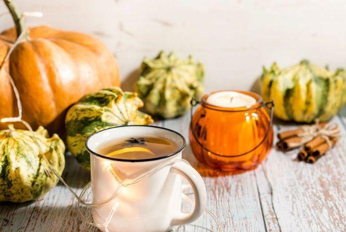 Autumn scene with lit candle mug gourds pumpkins and cinnamon arranged on rustic wooden surface.