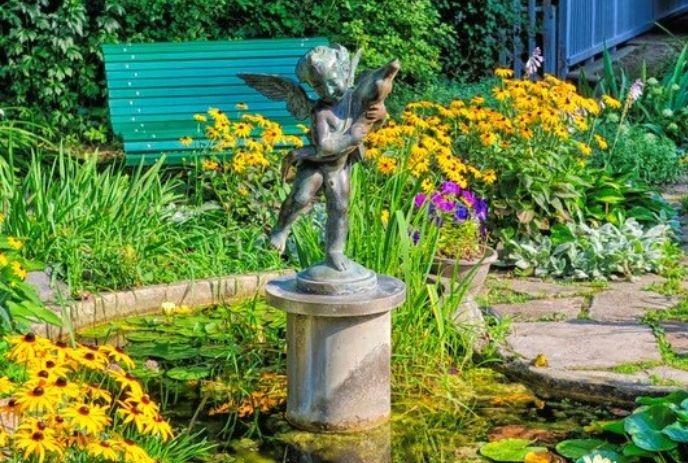 Bronze cherub statue stands above pond with lilies amid bright garden flowers and green foliage at Eldon House.
