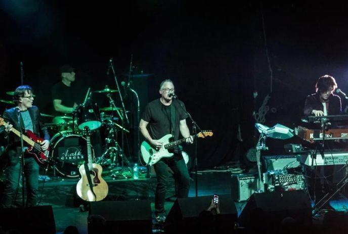 Chalk Circle performing live on stage with guitar bass drums and keyboards under dim green blue concert lighting.