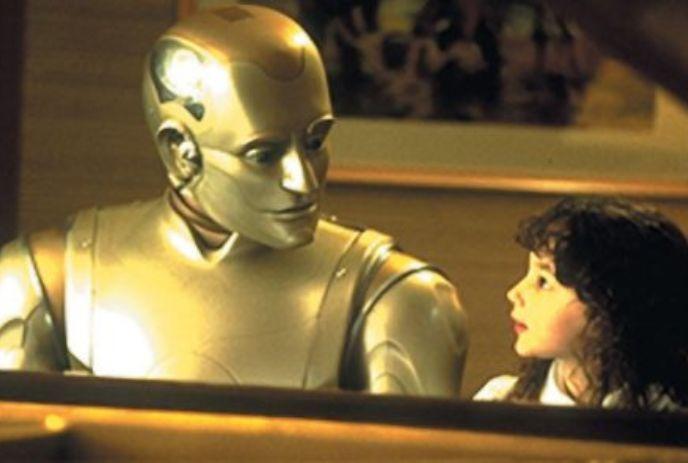Gold humanoid robot sitting beside child at piano with both looking at each other in warm indoor setting.