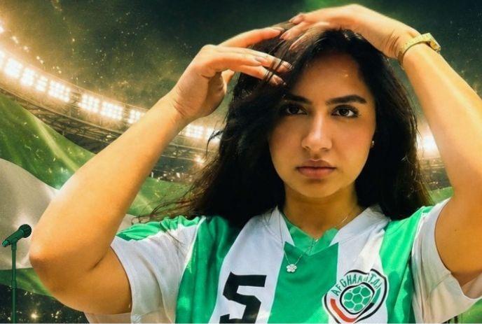 Zar The Star in green and white soccer jersey adjusting hair with stadium lights flag and microphone in background.