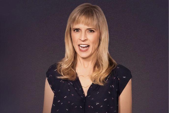 Maria Bamford against dark background wearing patterned shirt under a dark background.