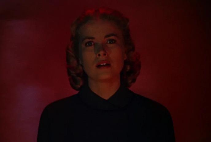 A person stands looking straight ahead with a red background behind them.