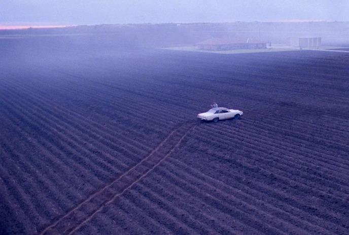 A lone white vehicle sits in the middle of a field.