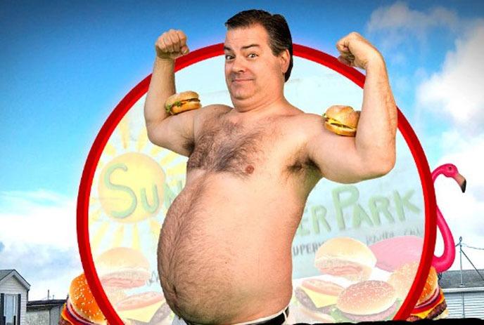 Randy, shirtless, flexing his muscles with cheeseburgers on his arms.