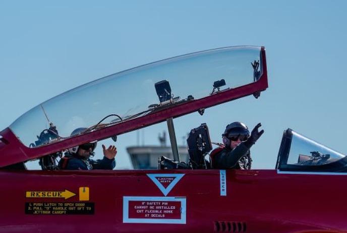 Two pilots waving from inside a plane cockpit.