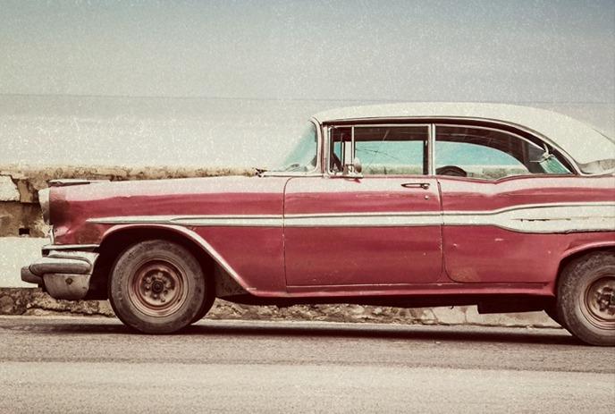 A vintage red car with a white roof is parked beside a weathered stone wall.