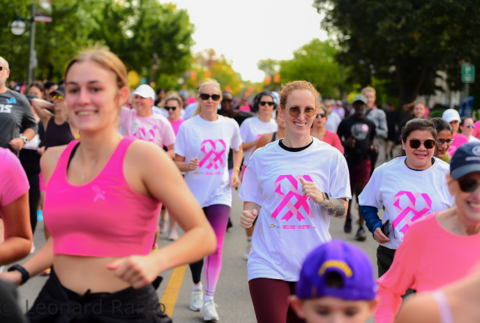 Crowd in pink and white shirts participates in outdoor charity run along tree lined city street in bright daylight.