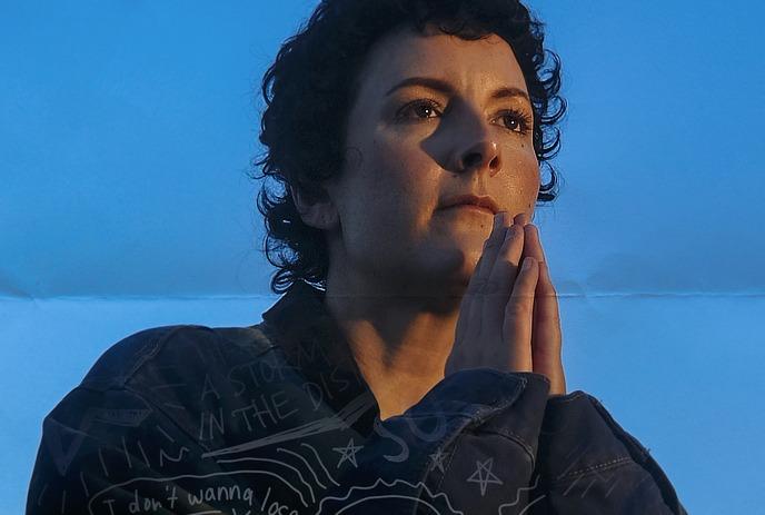 Ria Mae gazes ahead with a calm, reflective expression, wearing a denim jacket and short curls.