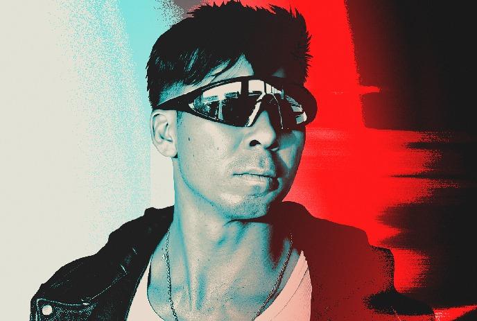 Artist in leather jacket with tinted glasses framed by split cyan and red lighting backdrop.