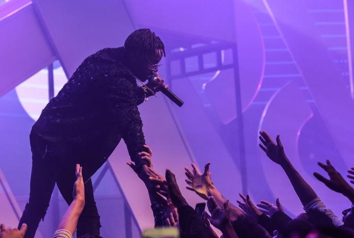 Roy Wood$ performing on stage, reaching out towards the crowd with a microphone in his hand.