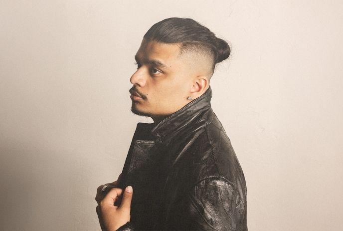 Artist in side profile wears black leather jacket, under an off-white background.