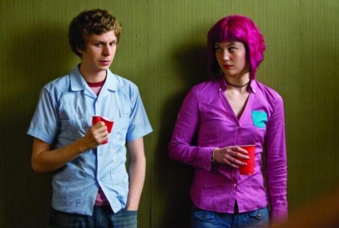 Scott and Ramona stand awkwardly against a green wall at a party, each holding a red cup.